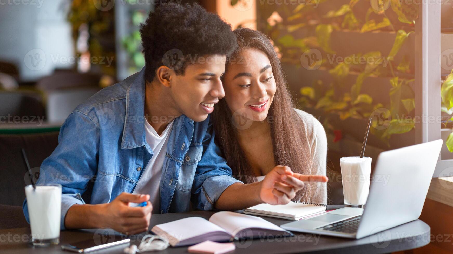 A young loving black couple sits at a table in a bustling cafe, focused on the screen of a laptop. They appear engaged in conversation as they review information on the device. photo