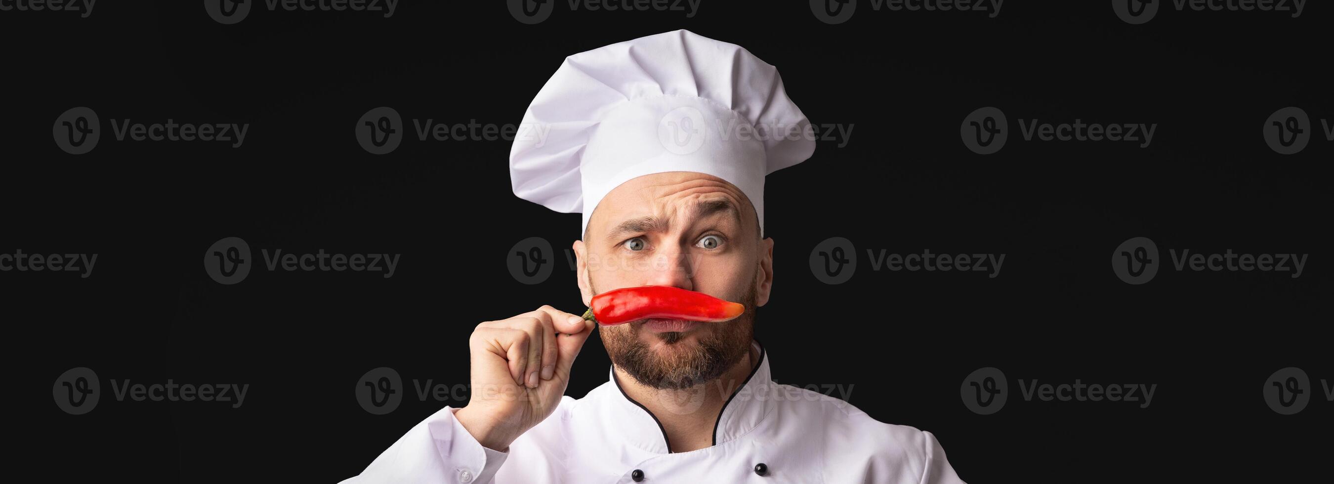 Chef Man Having Fun Posing With Red Chilli Pepper Holding It Like Moustaches Standing On Black Background. Panorama, Copy Space photo