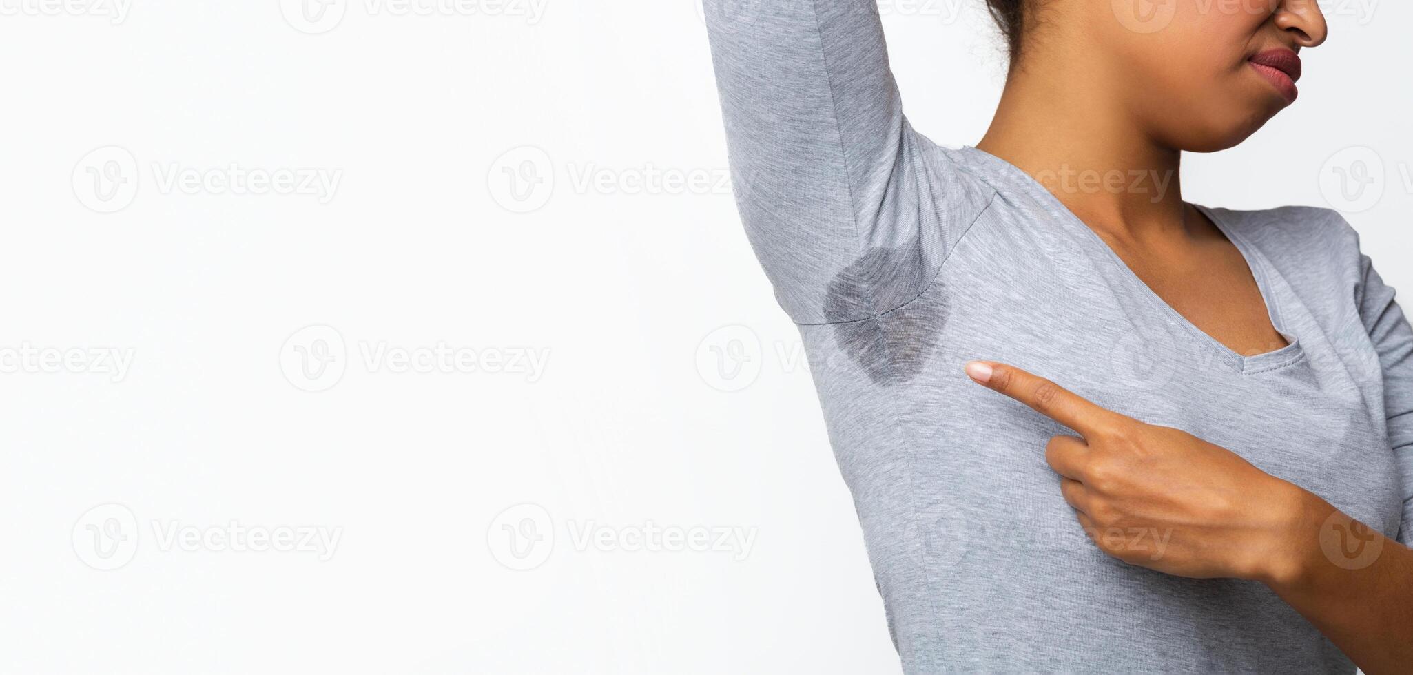 Cropped of young black woman looking at the sweaty shirt, grey background, copy space, wet armpit problem photo