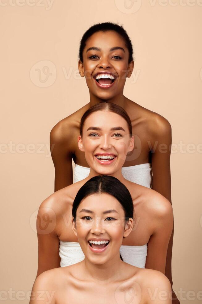 Cheerful African, Caucasian And Asian Girls Posing Wrapped In Bath Towels Over Gray Background. Studio Shot, Vertical photo