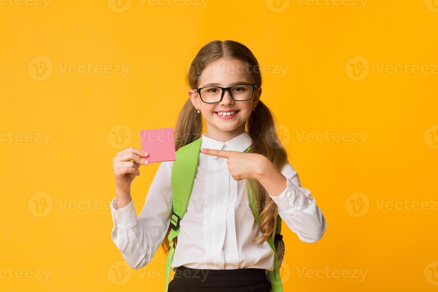 Take Notes. Schoolgirl Pointing Finger At Blank Paper Card Posing Over Yellow Background. Studio Shot photo