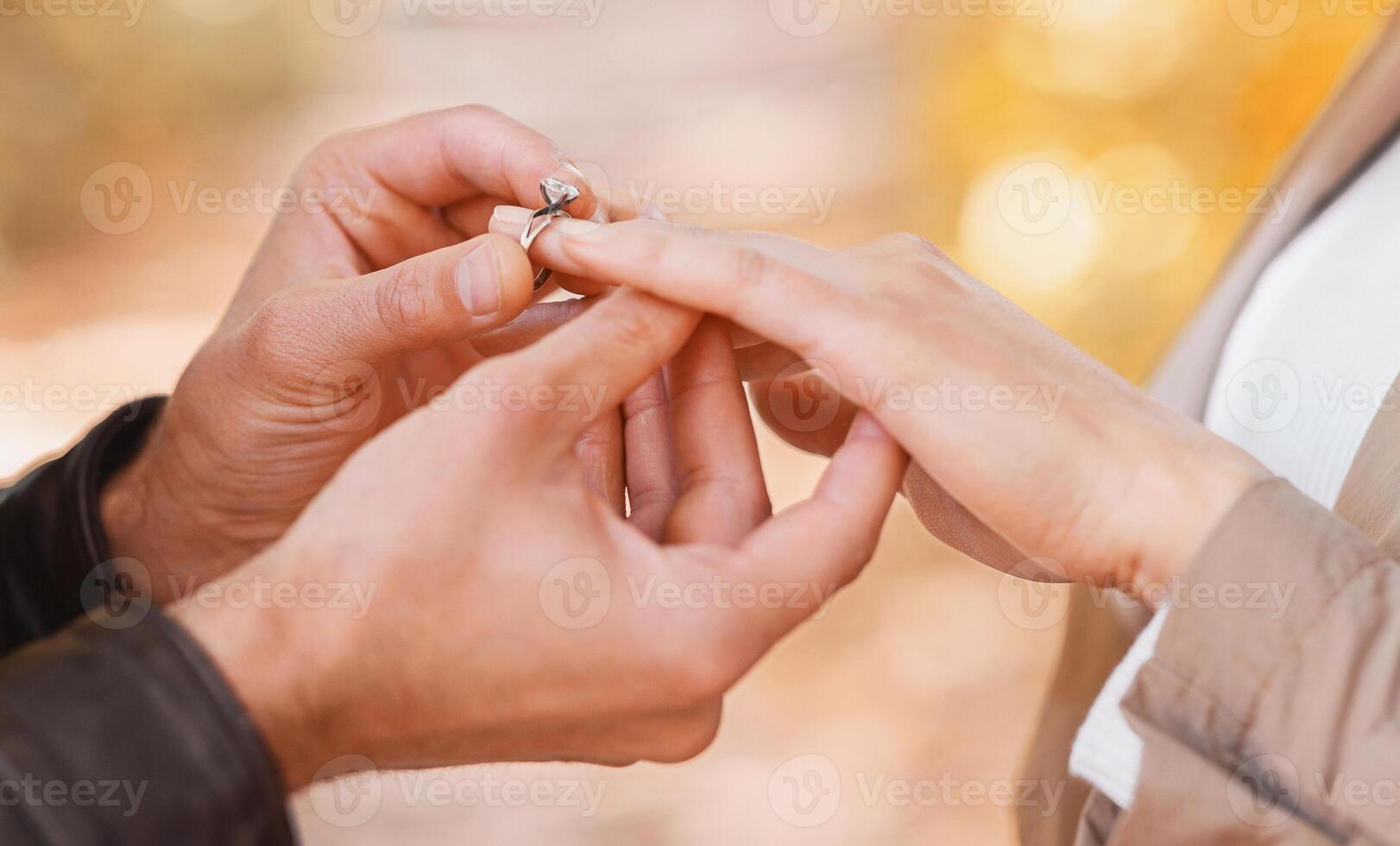 Close up of man putting engagement ring on woman's hand over blurred autumn forest background photo