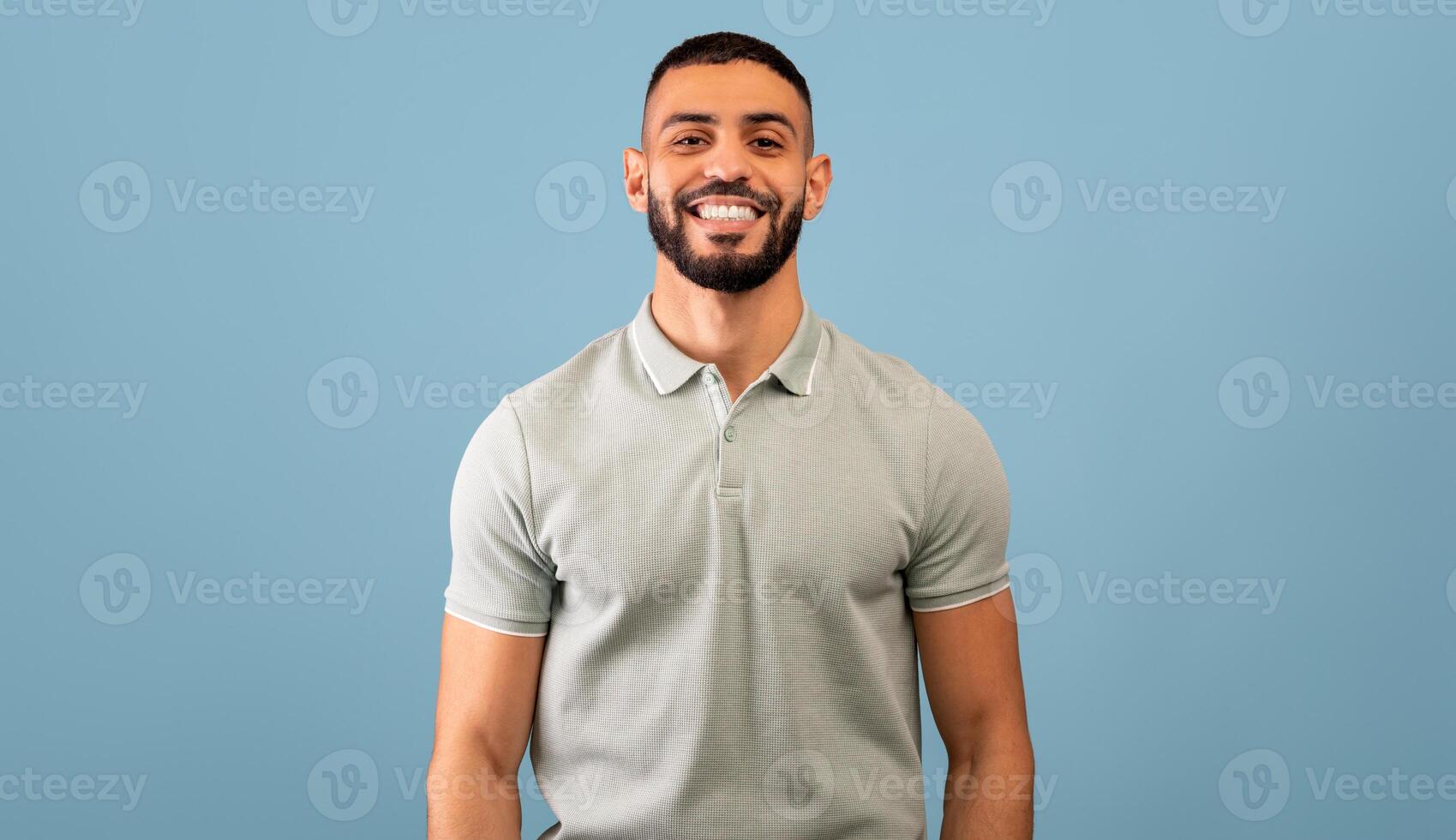 Portrait of happy arabic guy smiling at camera over blue studio background, copy space. Handsome middle-eastern young man in casual showing positive emotions photo