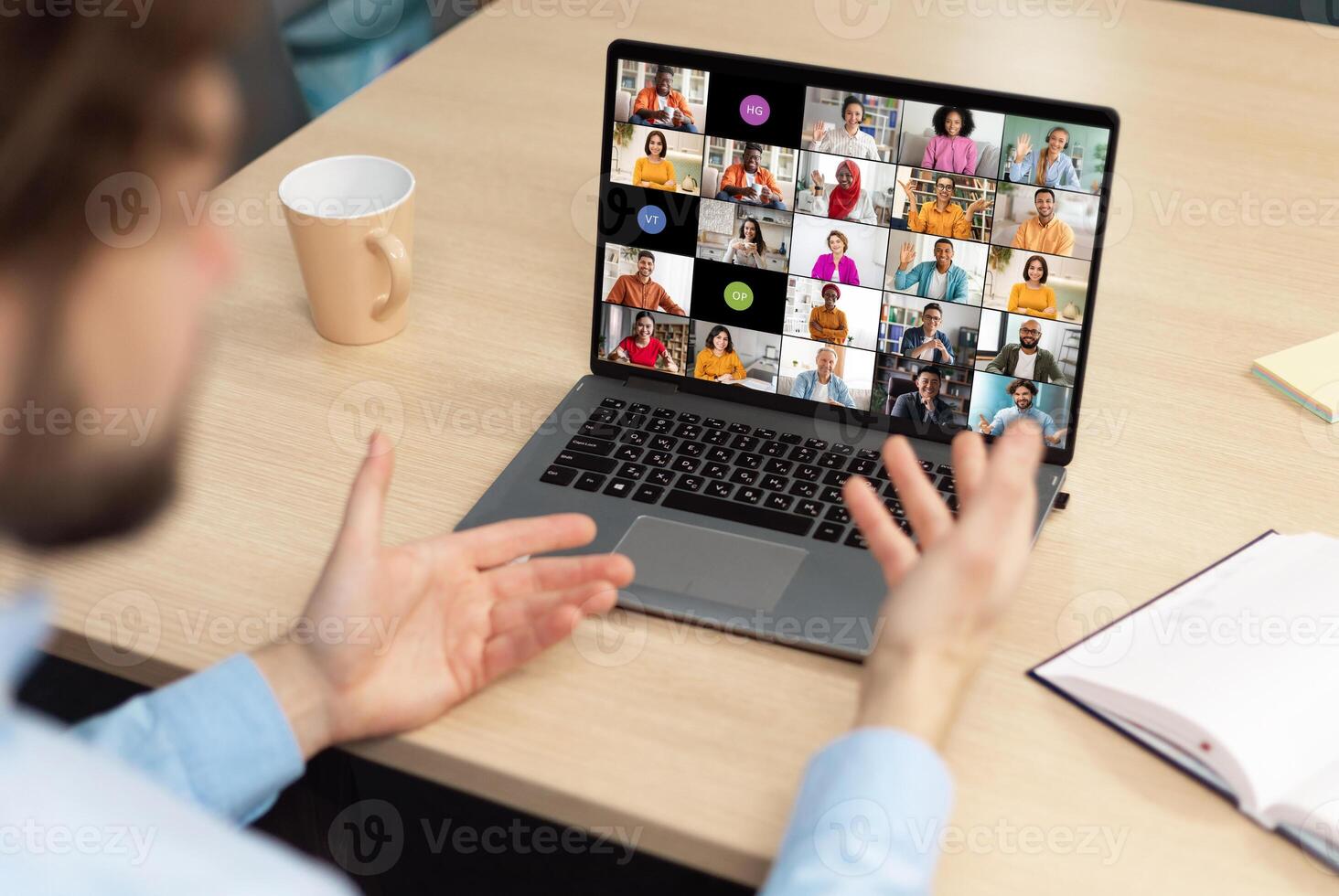 A man sits at a desk in front of a laptop, actively participating in a conference meeting with colleagues. His hands are raised, gesturing and engaging with the online participants. photo