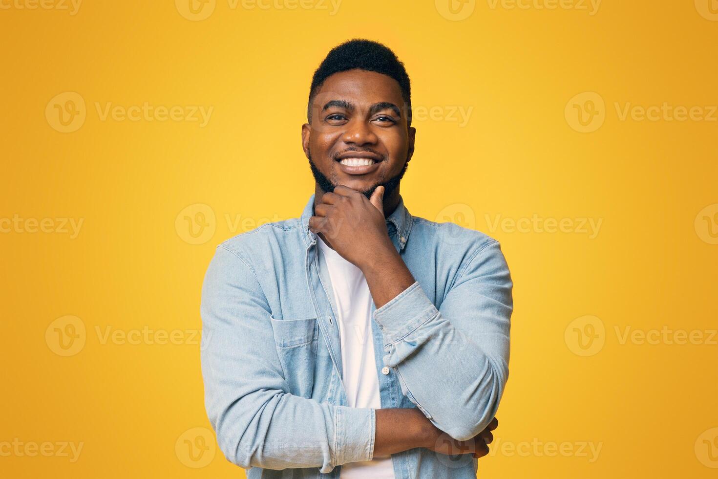 Portraif of handsome bearded african american man touching his chin and smiling over yellow studio background, copy space photo