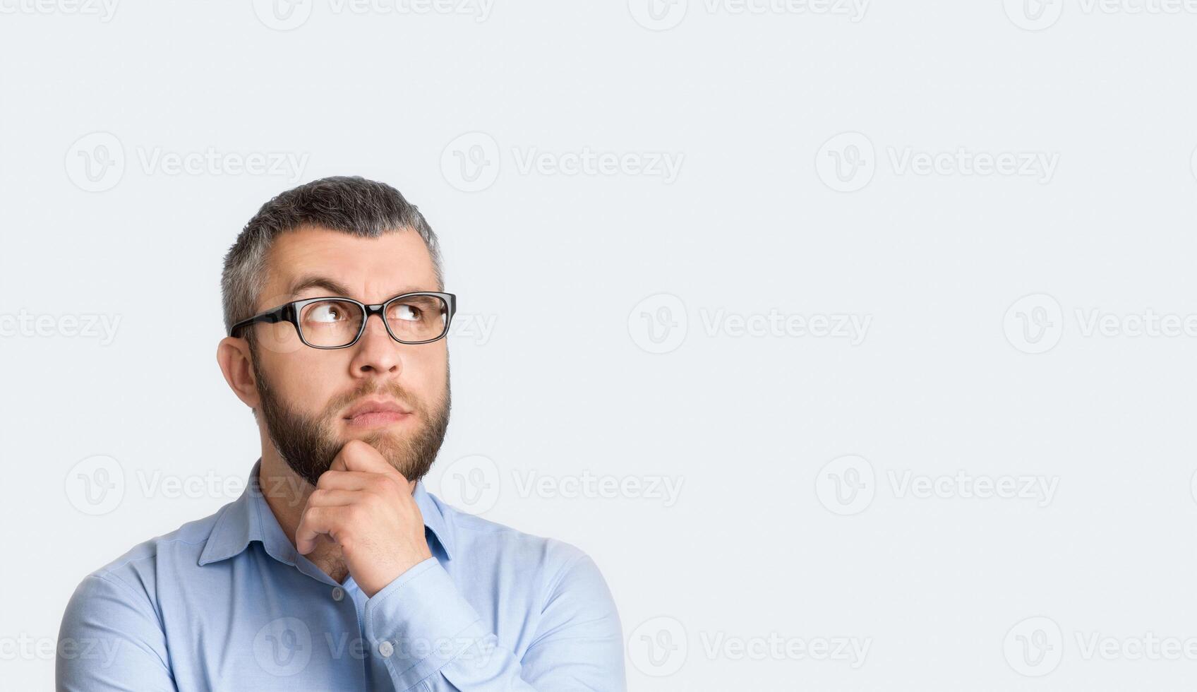 A man wearing glasses and a blue shirt is standing in the photo. He appears to be looking straight ahead with a neutral expression on his face, copy space photo