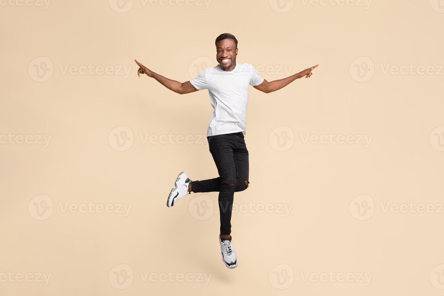 Cheerful Black Guy Jumping In Air Having Fun Posing Over Yellow Background. Studio Shot photo