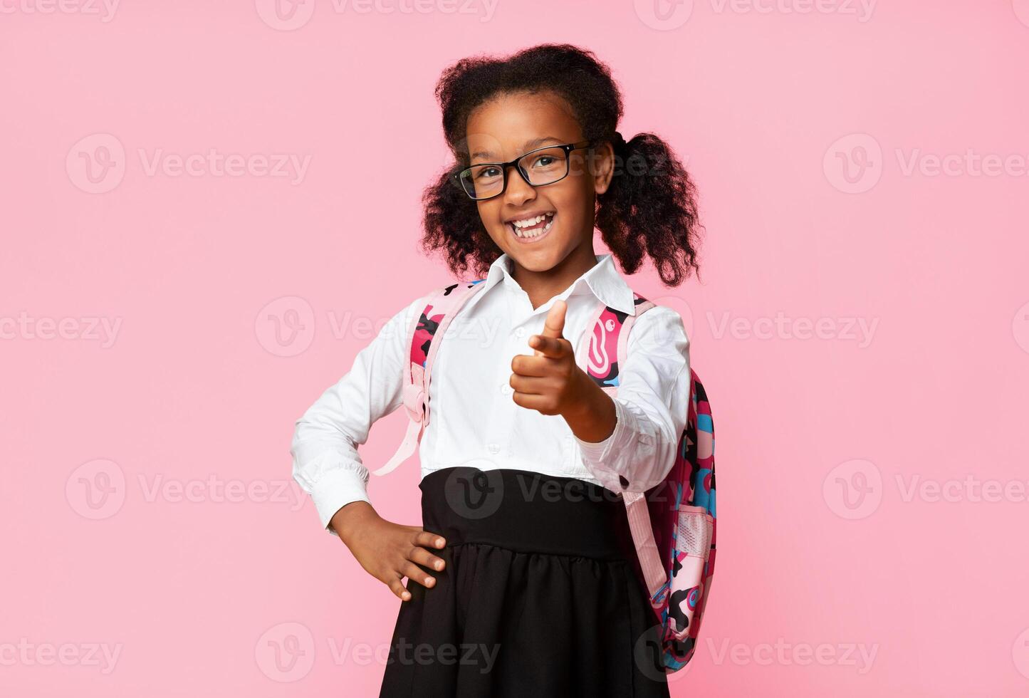 Hey, you. Cute Afro Elementary Student Girl Pointing Finger At Camera On Yellow Background In Studio. Copy Space photo