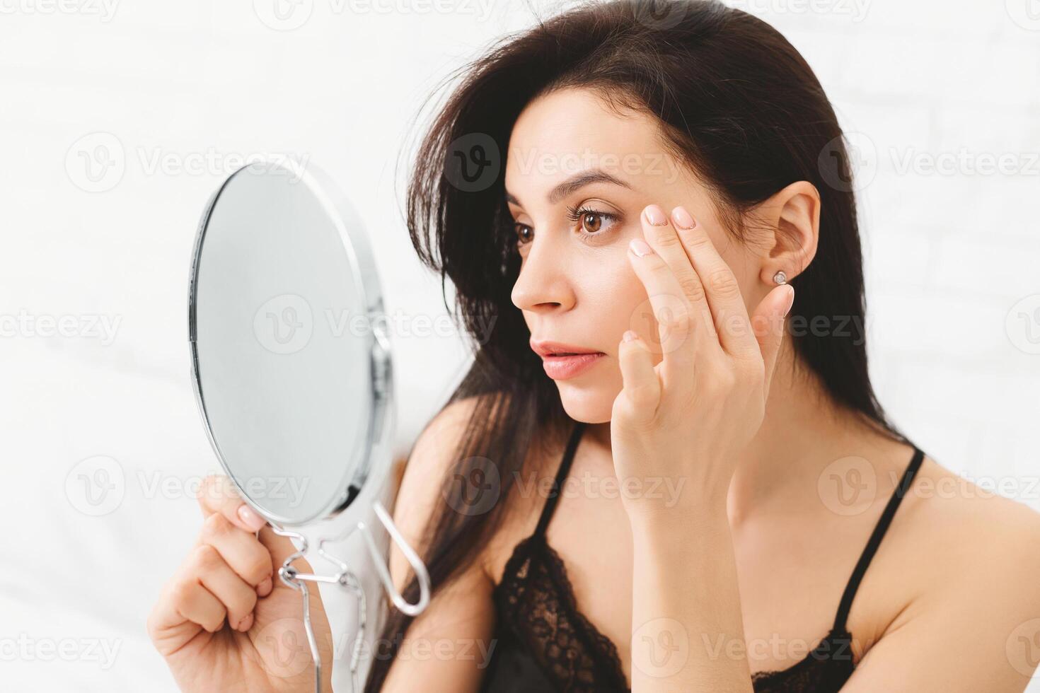 A woman is standing in front of a mirror, closely inspecting her reflection. She appears focused and thoughtful as she examines her features. photo