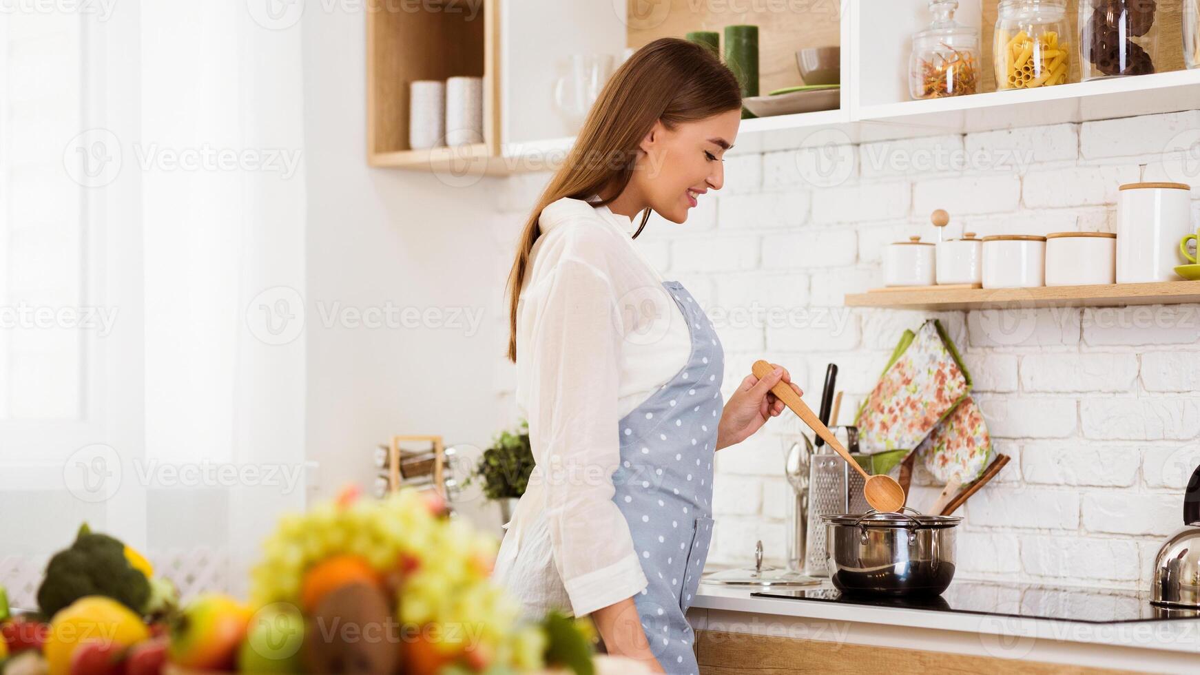 A woman in a polka dot apron cooks on a stovetop in a modern kitchen. photo