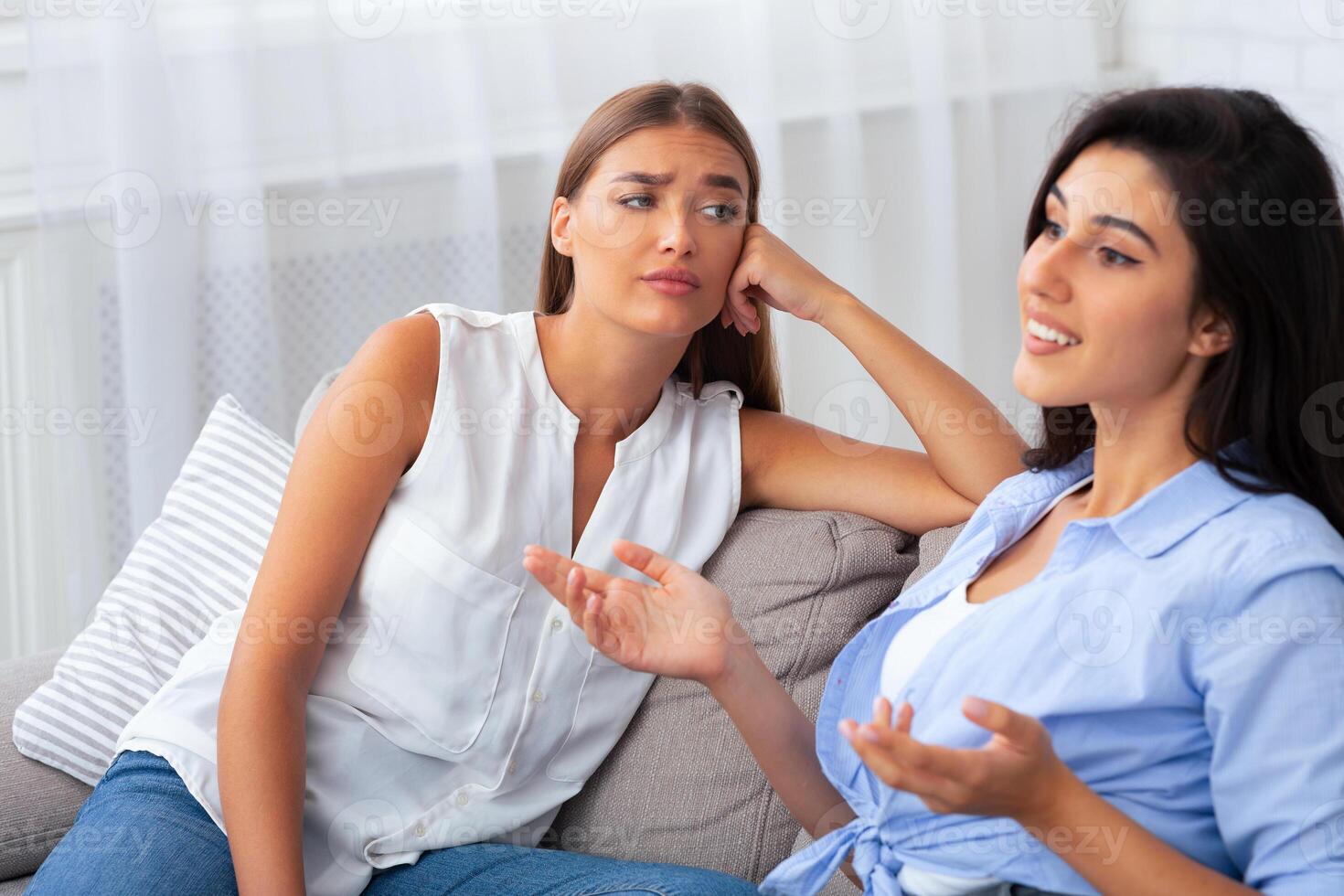 Envy. Jealous Girl Listening To Her Friend Talking About Her Great Life Sitting On Couch At Home. Selective Focus photo