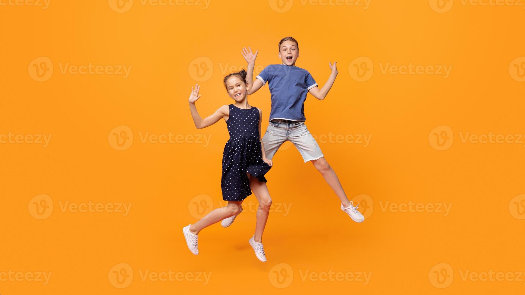 Happy little girl and boy jumping for joy together on orange studio background photo