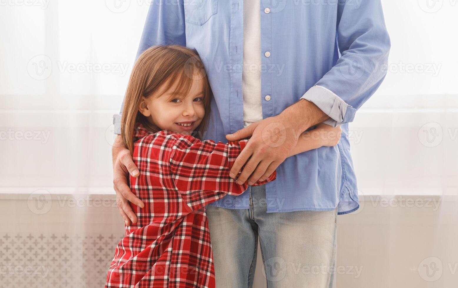 You are my hero. Sweet smiling little girl hugging her dad at home, staying next to window, close up, copy space photo