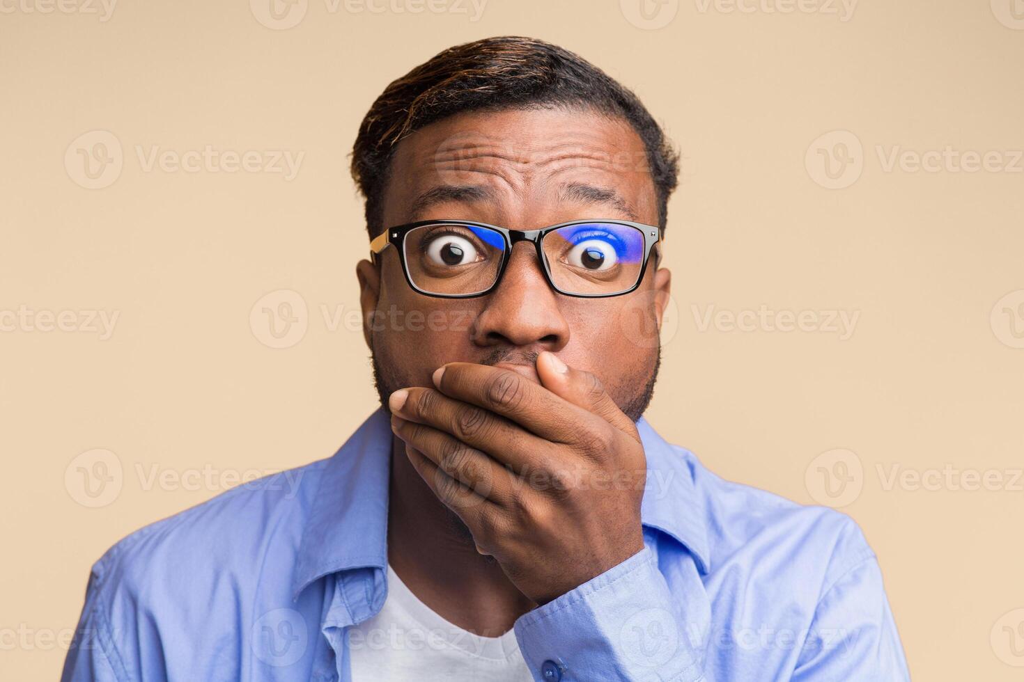 Omg. Shocked African American Guy Covering Mouth With Hand Looking At Camera Over Yellow Studio Background. photo