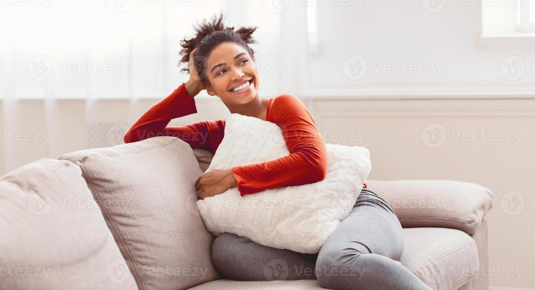 Home Comfort. Happy African American Woman Relaxing Sitting On Sofa Embracing Pillow Enjoying Weekend Indoor. Panorama photo