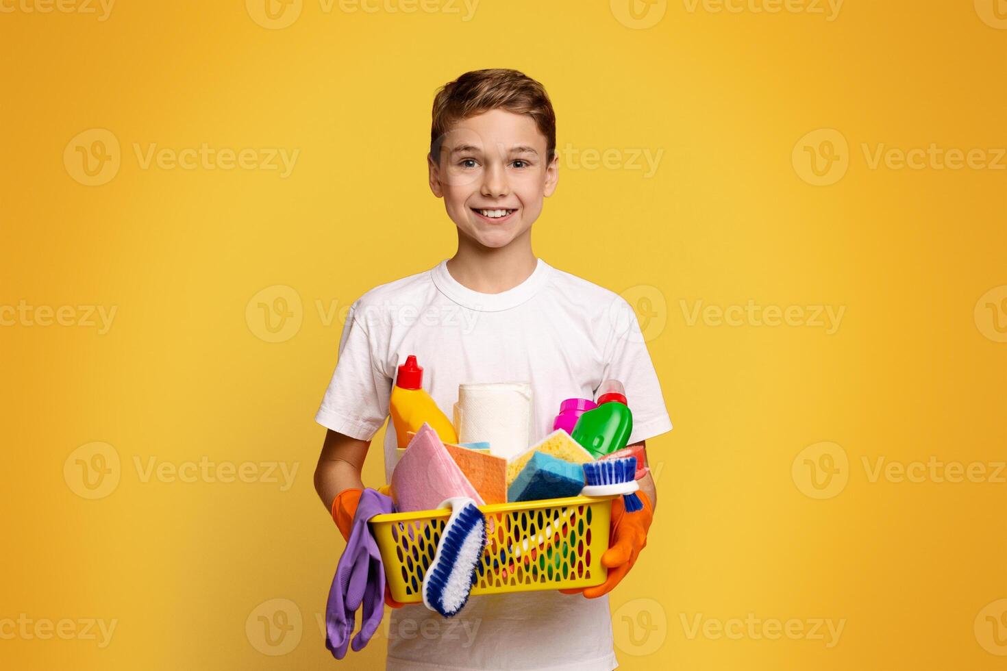 Young cleaner. Cute boy holding set of cleaning supplies, orange studio background photo