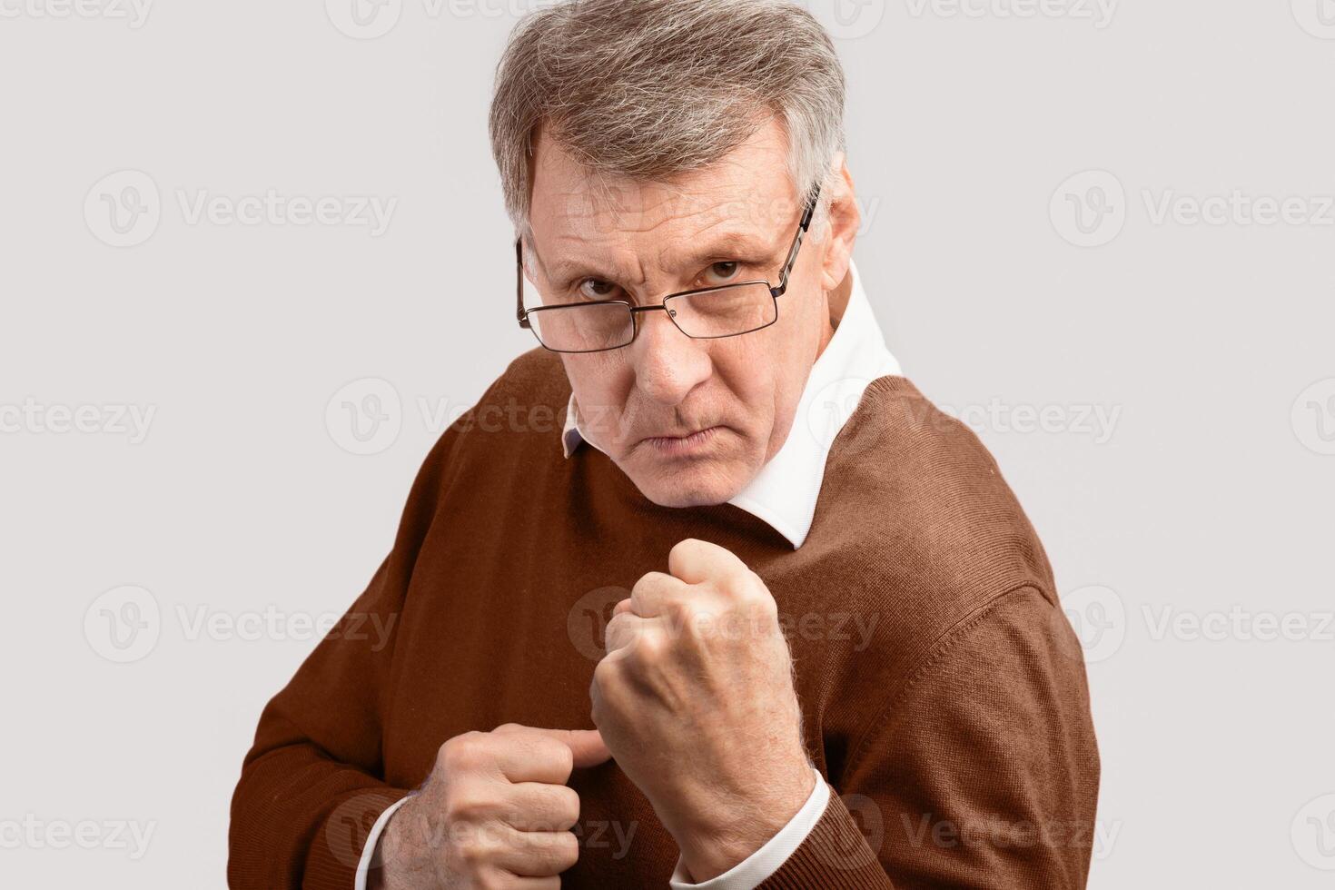 Aggressive Senior Man Clenching Fists Standing In Ready-To-Fight Position Looking At Camera Over Gray Studio Background. photo