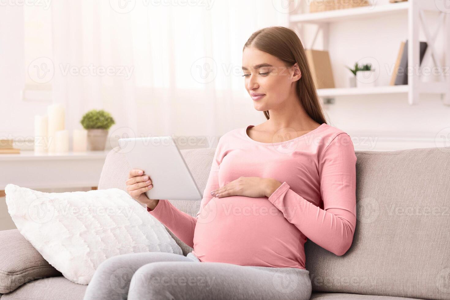 Content Pregnant Woman Using Digital Tablet Computer Reading E-Book Relaxing Sitting On Couch At Home photo