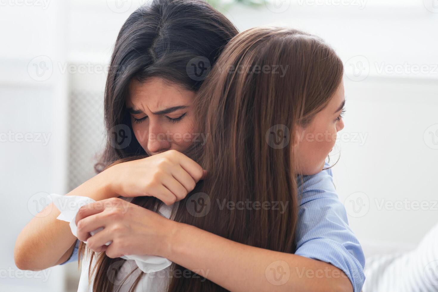Friendship And Support. Depressed Girl Crying Hugging Her Compassionate Friend Complaining About Problems Sitting On Couch Indoor. Selective Focus photo