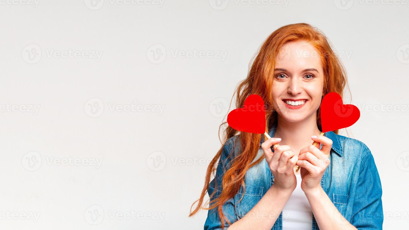 A woman is standing and holding two heart-shaped objects in front of her face, panorama with copy space, white background photo