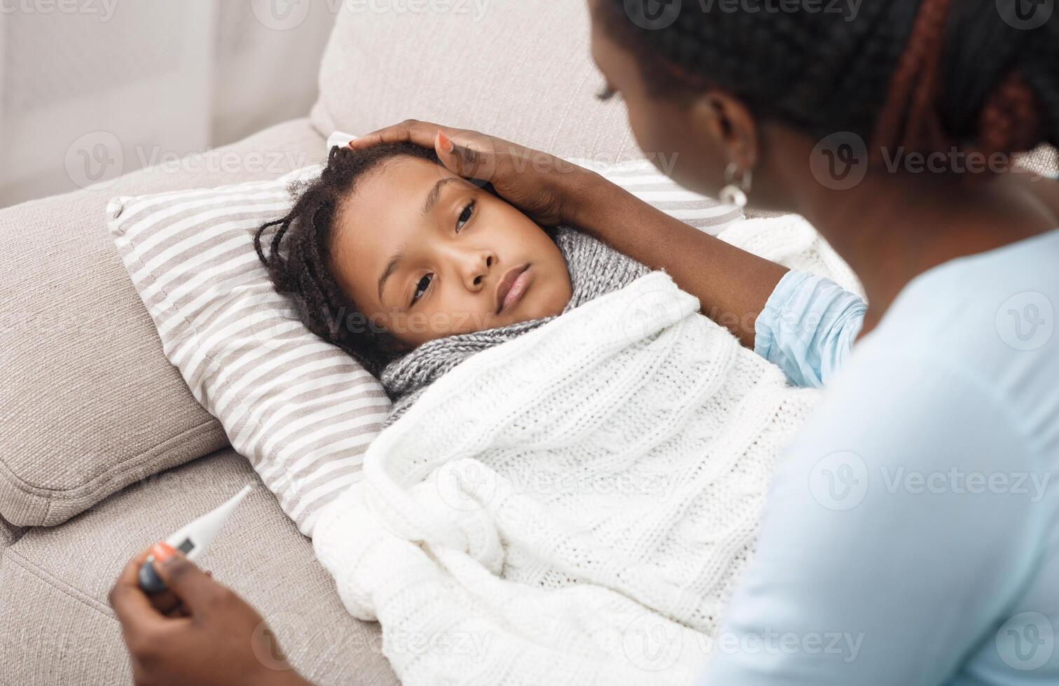 Fever Concept. Sick child in bed, mother holding thermometer, comforting poor girl photo