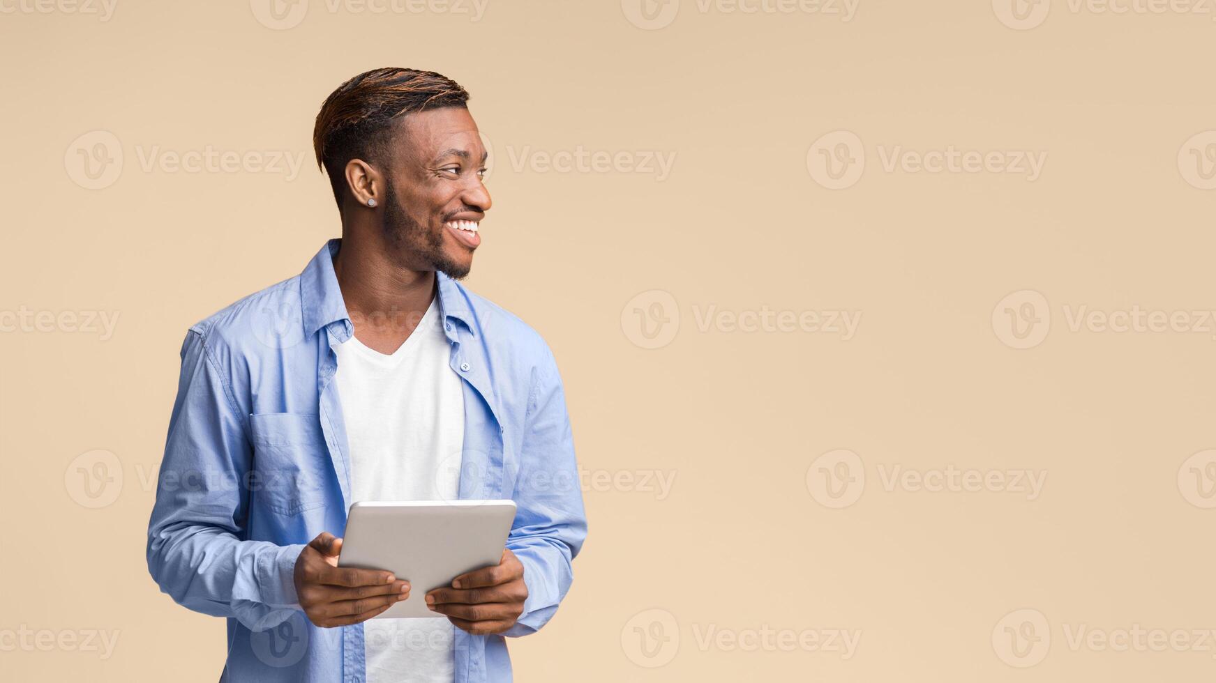 Happy African American Man Holding Tablet Computer Looking Aside Standing On Yellow Background In Studio. Panorama, Free Space photo
