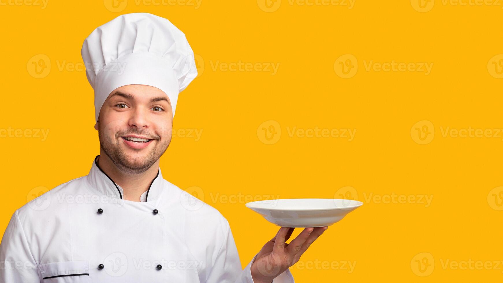 Smiling Chef Man Serving Dish Holding Empty Plate Standing Over Yellow Background. Studio Shot photo