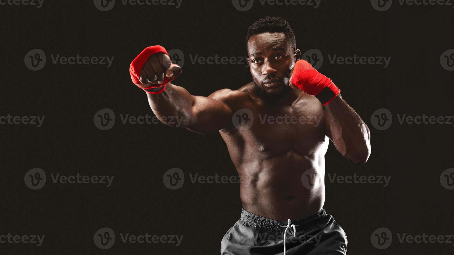A muscular man with red hand wraps practices boxing in front of a black background. photo