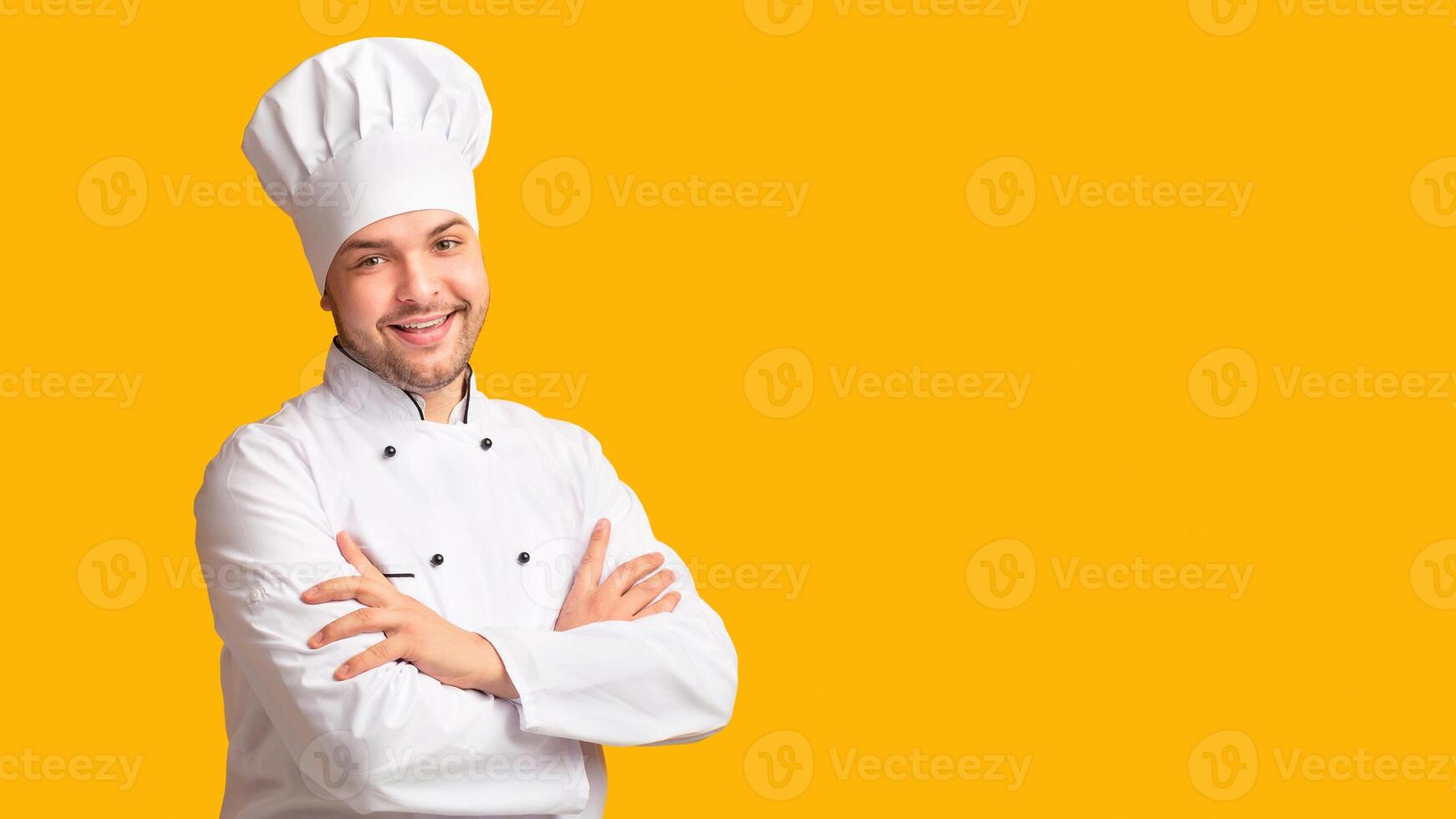Professional Cheef. Cook Guy Smiling At Camera Posing Crossing Hands Standing In Studio On Yellow Background. Panorama photo