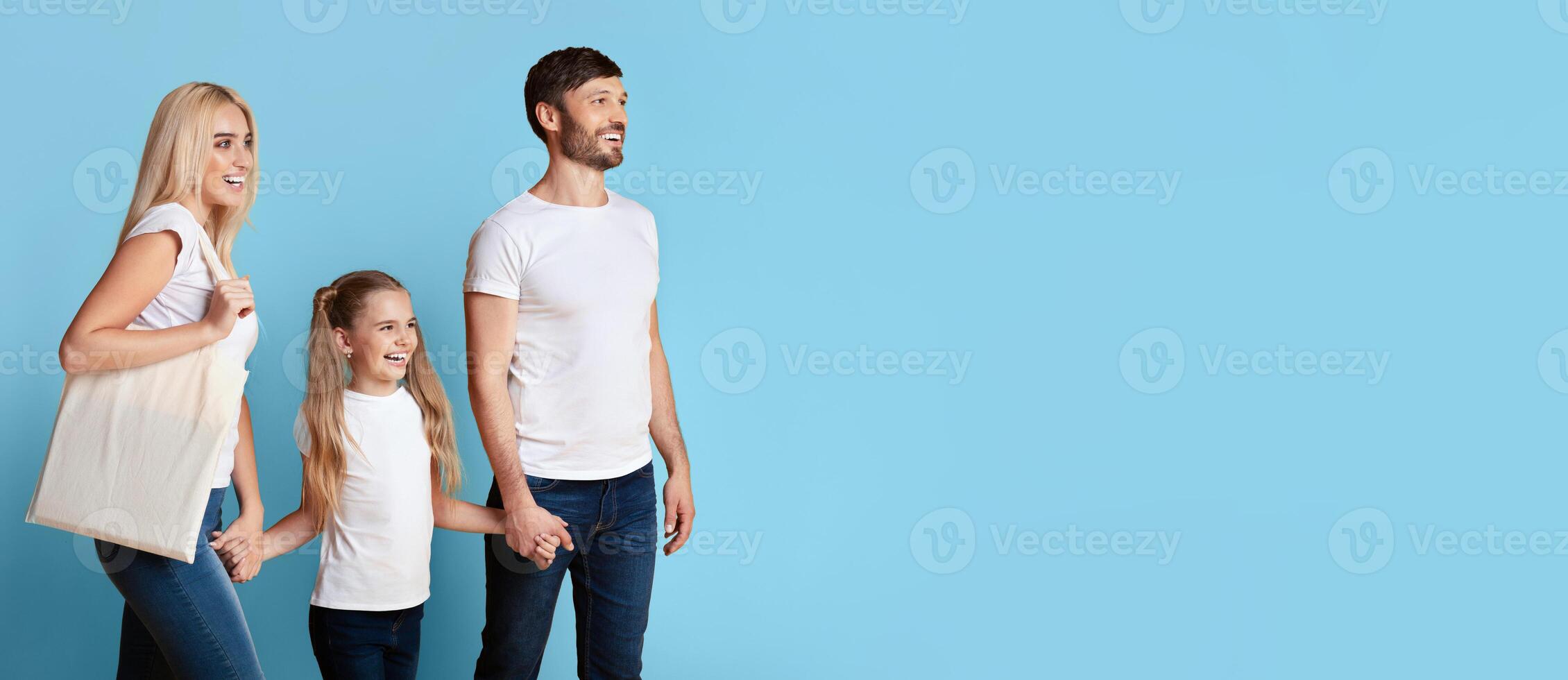 A family of three, a mother, father, and young daughter, walk hand-in-hand against a light blue background. The family appears to be happy and enjoying their time together, copy space photo