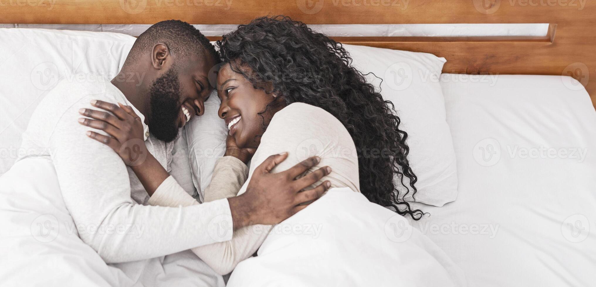 Lovely morning. Black millennial couple cuddling in bed at home, resting, and enjoying weekend together photo
