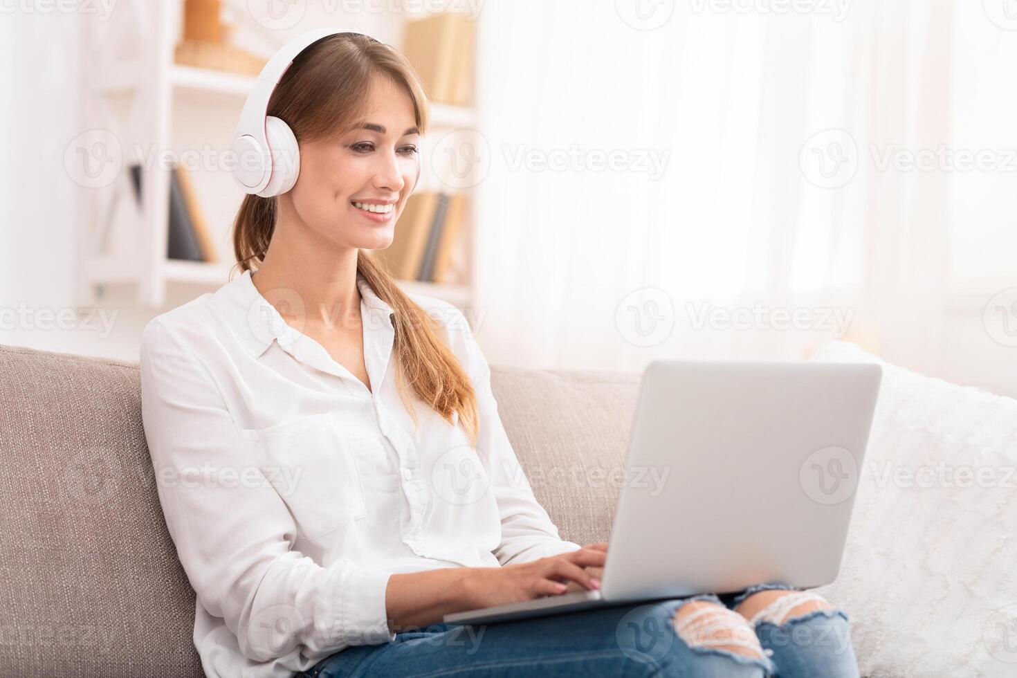 Freelance Career. Cheerful Lady In Wireless Headphones Working On Laptop Computer Sitting On Sofa At Home. Selective Focus photo