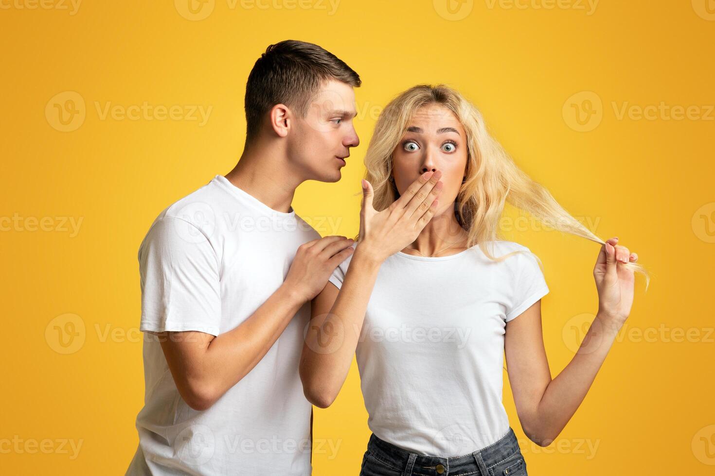 Unbelievable. Guy whispering secret or gossip to surprised girl, yellow background with copy space photo