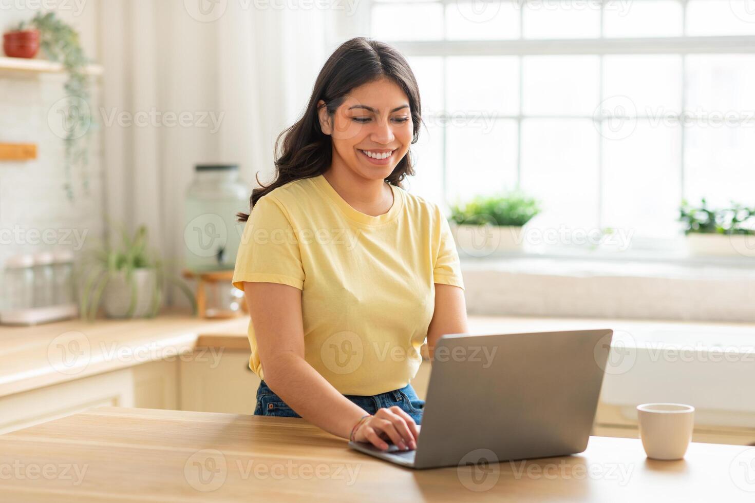 A middle eastern woman is sitting at a table, focused on her laptop computer. She appears engrossed in her work, typing and scrolling on the screen. photo
