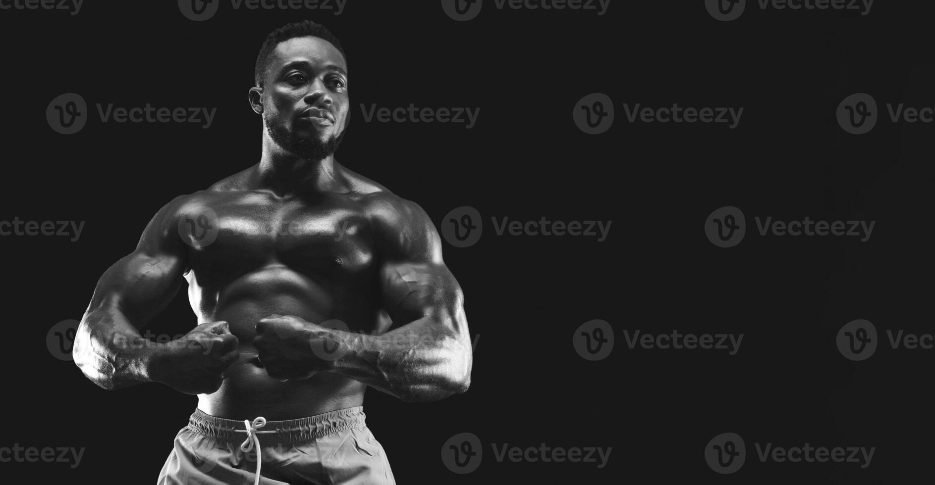A muscular man poses in a dark studio, flexing his biceps and showing off his toned physique. photo