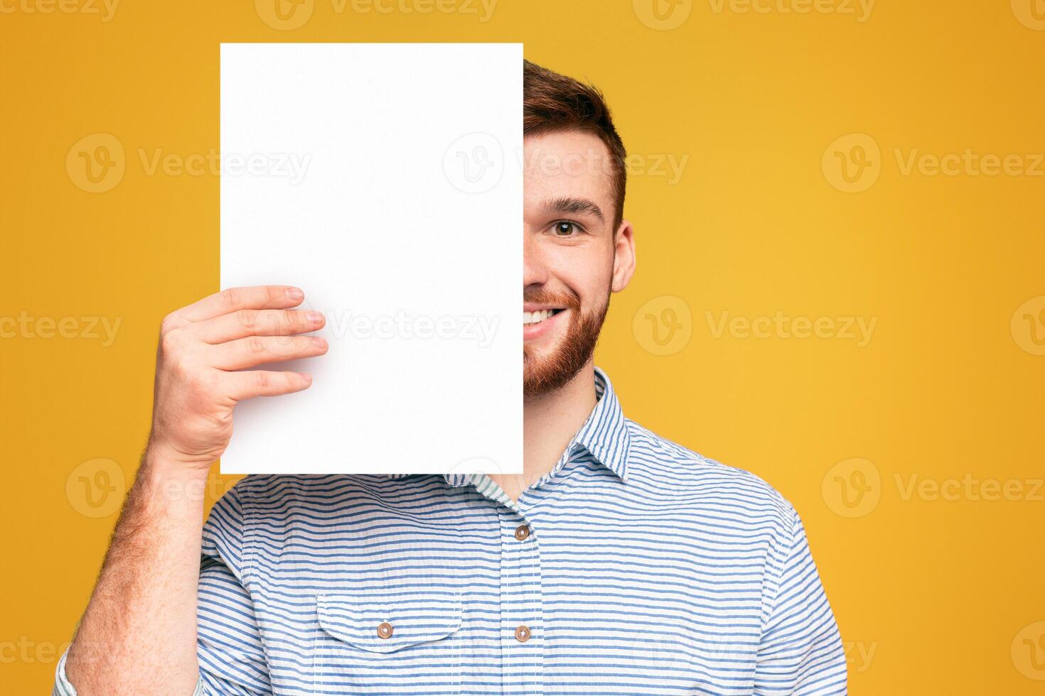 A man standing and holding up a white piece of paper in front of him, mockup copy space, yellow studio background photo