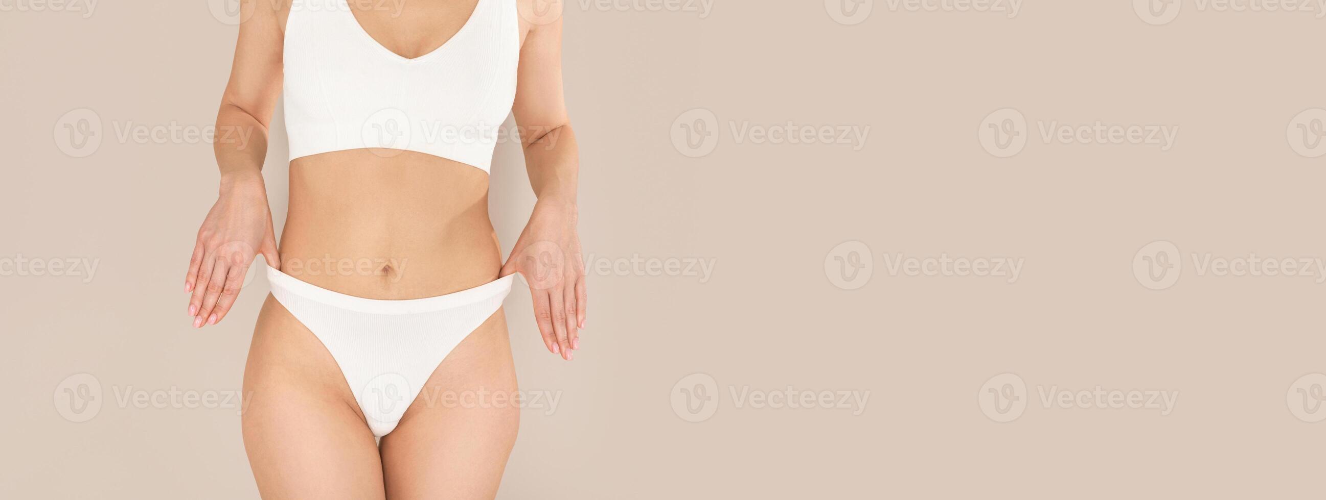 Unrecognizable well fit young woman posing in white underwear, showing smooth sexy body without cellulite and stretch marks, adjusting her panties, isolated, studio background, copy space photo