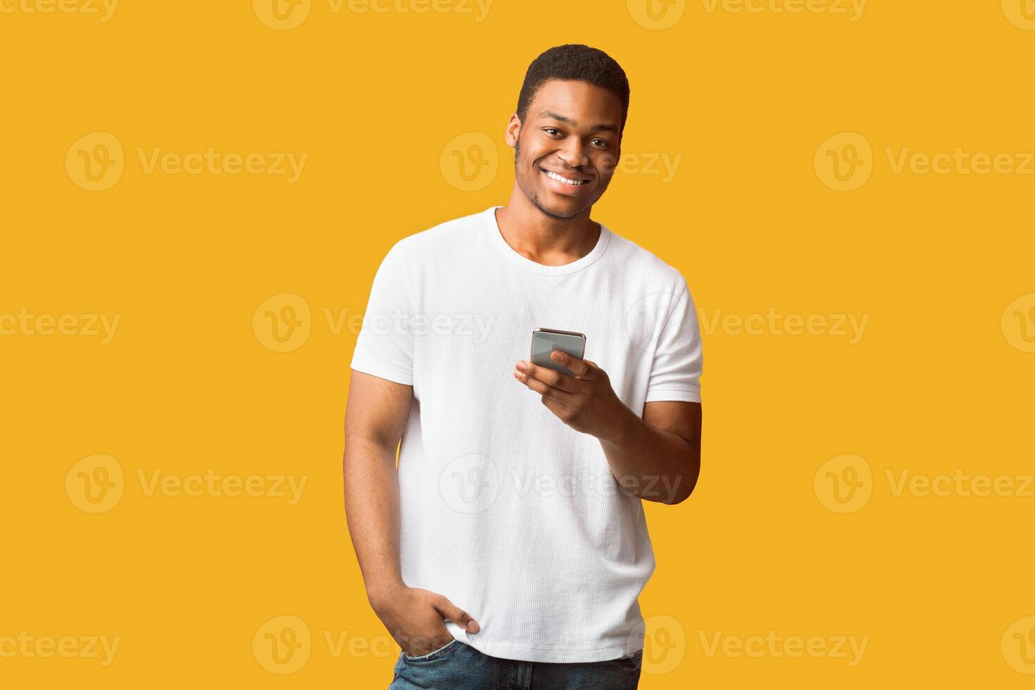 Money Transfer Online. Happy afro guy using mobile phone, looking at camera, copyspace, orange wall photo