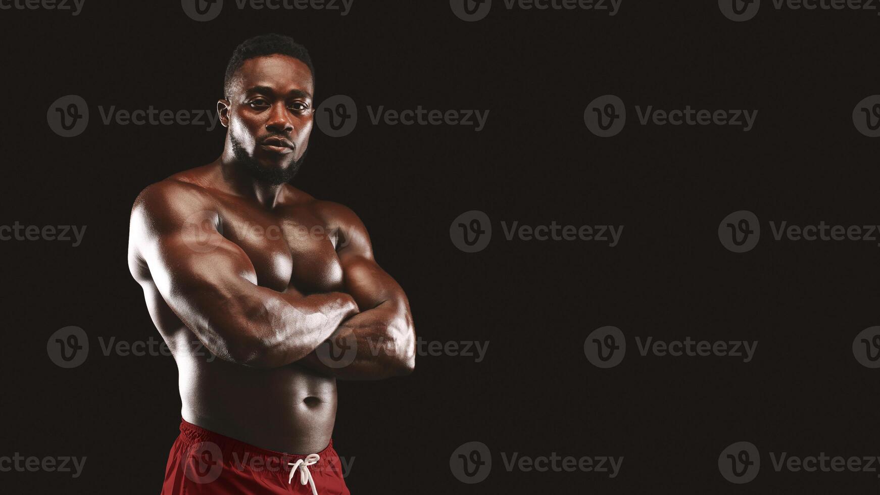 A muscular man poses with arms crossed in front of a black background. photo