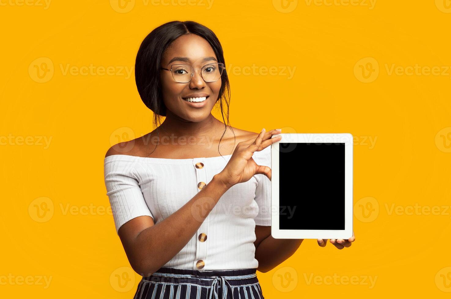 Afro Young Lady Showing Digital Tablet Empty Screen Smiling At Camera Standing On Orange Background In Studio. Mockup photo