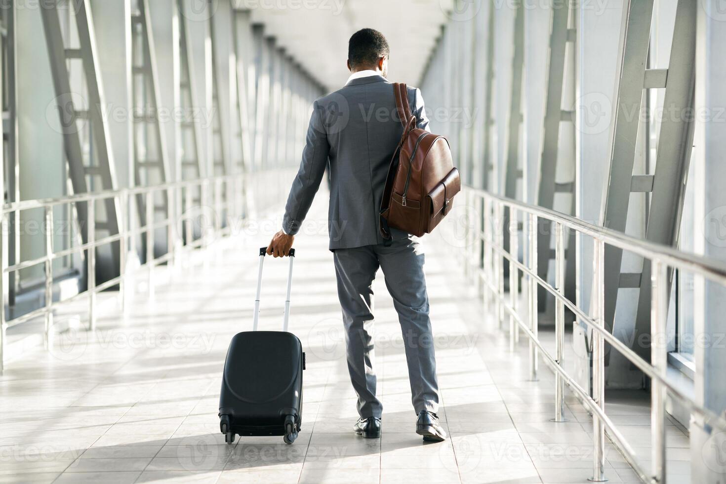 A corporate traveler with luggage is seen at an airport. The mood is focused and professional, with a modern airport setting that emphasizes travel and business, back view photo
