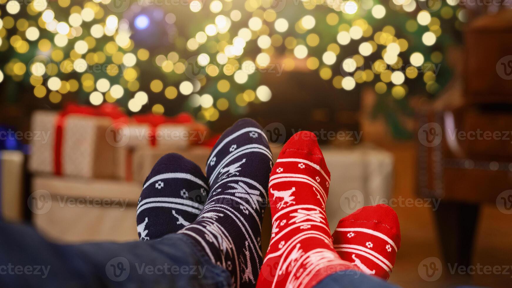 Couple relax. Two pair of feet in colorful ornamented Christmas socks over blurred Xmas room background, selective focus photo