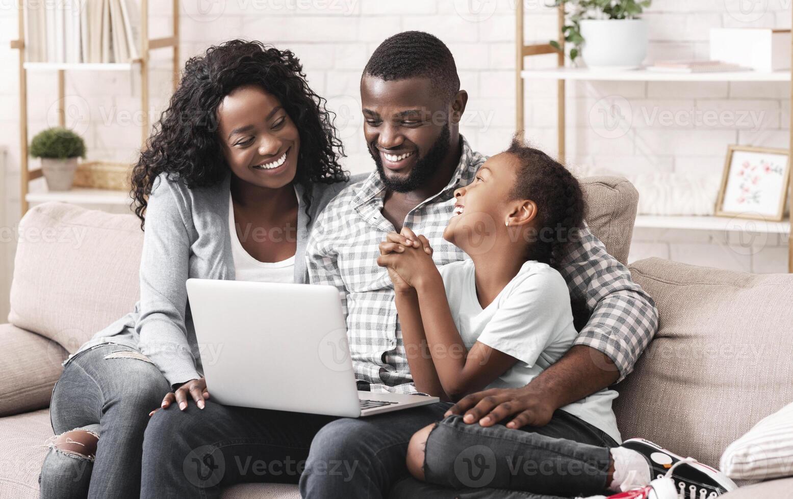 Happy african american family of three watching movie on laptop together, sitting on sofa at home. photo