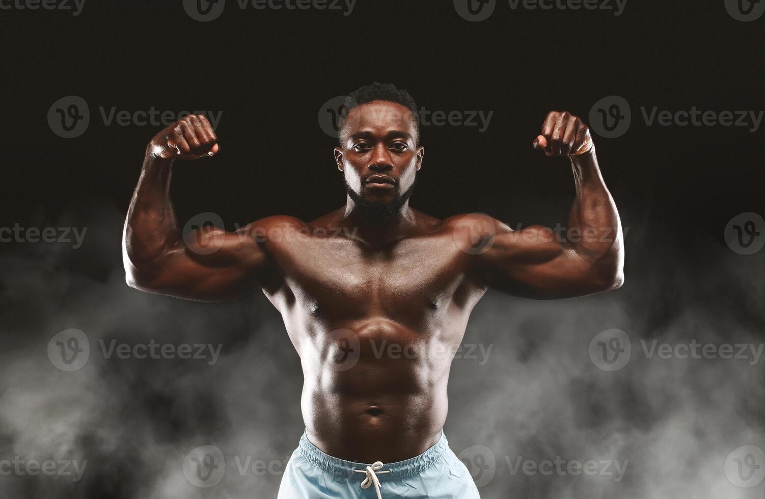 A muscular man flexes his biceps, showcasing his strength and physique against a dark background with subtle smoke effects. photo