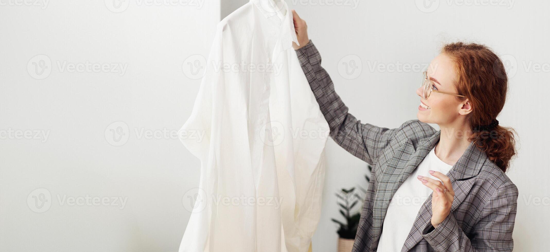 Happy Red-Haired Fashionista In Glasses Buying New Clothes In Showroom. Copy Space For Text photo