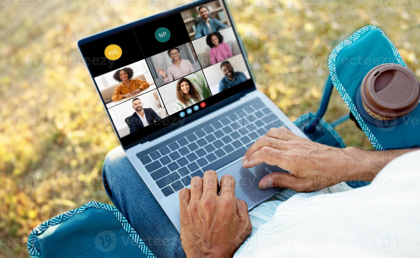 Senior man is sitting outside, participating in a virtual business meeting on his laptop. Several colleagues are visible on the screen, engaging in conversation. photo