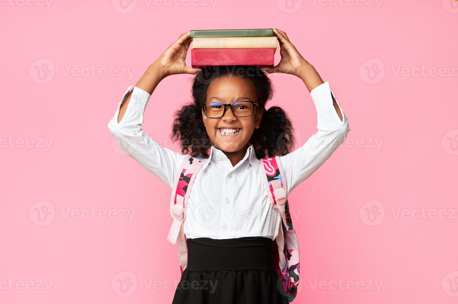 Cute Black Schoolgirl Holding Books On Head Over Yellow Background. Back To School Concept, Studio Shot photo