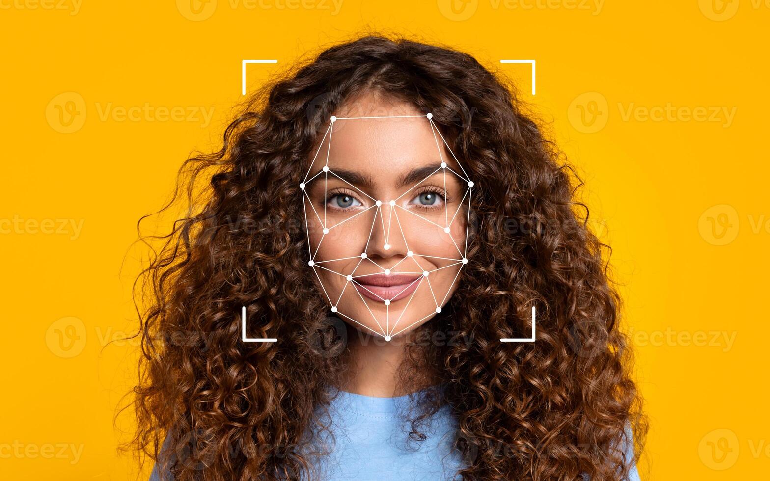 A young woman with long curly hair smiles confidently, framed by a bright yellow backdrop, showcasing a cheerful expression. photo