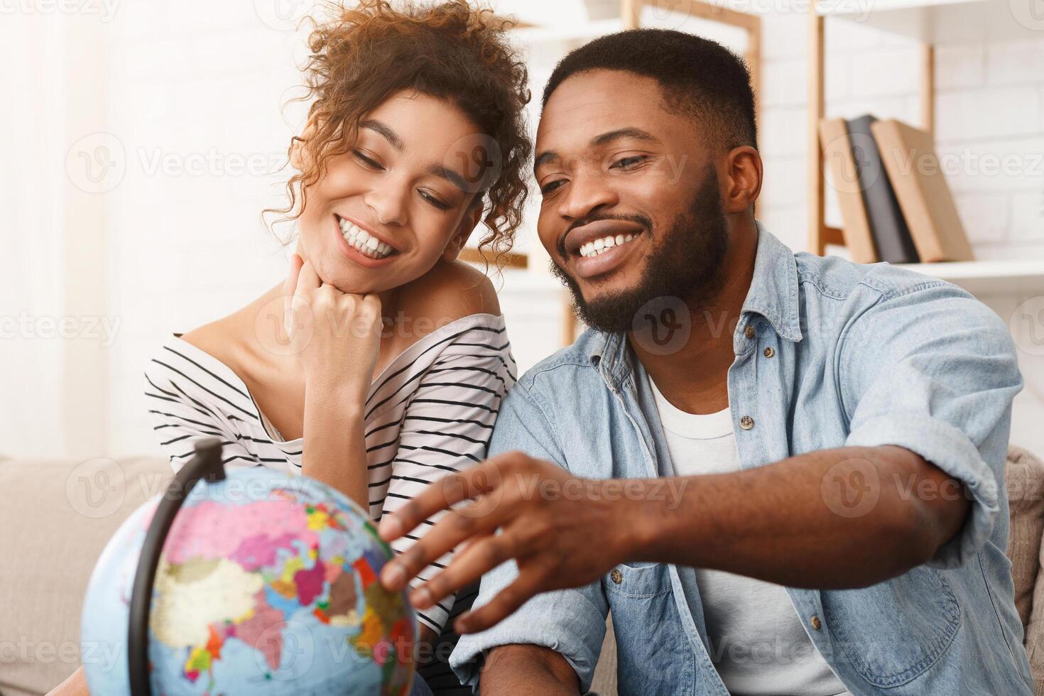 African-american couple dreaming of travel, looking at globe and choosing place for vacation photo