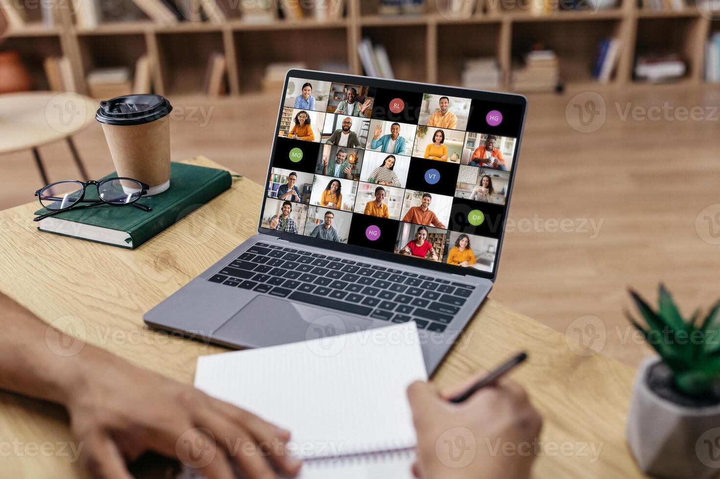 A person sits at a desk, taking notes on a notepad while participating in a conference meeting on their laptop computer. photo